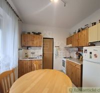Kuchyně v rodinném domě s dřevěnými skříňkami, jídelní stůl, lednička, židle.