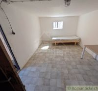 Pokoj v rodinném domě s postelí, stolem a oknem, světlé stěny.