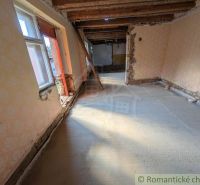 Interiér rodinného domu s odkrytými dřevěnými stropy a poškozenými stěnami.