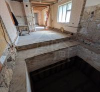 Interiér rodinného domu s odkrytým stropem a surovými stěnami v rekonstrukci.