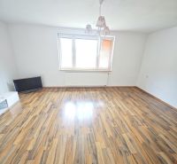 Prostorný obývací pokoj s podlahou s dřevěným dekorem a velkým oknem v 3-pokojovém bytě.