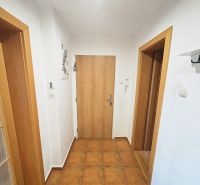 Chodba v 3-pokojovém bytě s keramickou dlažbou, bílými stěnami a dřevěnými dveřmi.