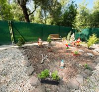 Zahrada s trpaslíky a lavičkou u chaty v Gabčíkovu, obklopená kameny a plotem.