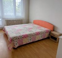 Ložnice s postelí a patchworkovým přehozem ve 2-pokojovém bytě, podlaha s dřevěným dekorem.