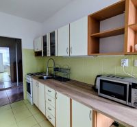 Kuchyně v 2-pokojovém bytě s mikrovlnkou a varnou deskou, směřující do další místnosti.