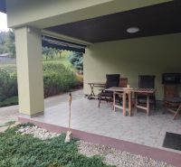 Terasa rodinného domu v Trebostově s dřevěným zahradním nábytkem a upravenou zelení.
