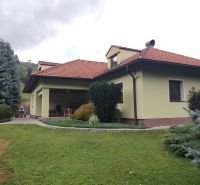 Rodinný dům v Trebostově se zahradou, trávníkem, terasou a stromy na dvoře.
