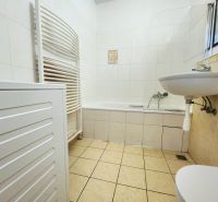 Koupelna v 2-pokojovém bytě s vanou, umyvadlem a pračkou, obložená bílými obkladačkami.