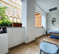 Balkon v 2-pokojovém bytě s květináči a dřevěným nábytkem.