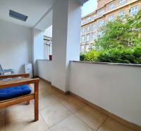 Balkon 2-pokojového bytu s výhledem na zeleň a budovu, posezení s židlemi.