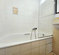 Koupelna v 2-pokojovém bytě s vanou a umyvadlem, obložená světlými dlaždicemi.