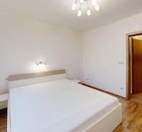 Světlá ložnice s postelí, podlahou s dřevěným dekorem a minimalistickým osvětlením v 3-pokojovém bytě.