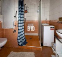 Koupelna v 3-pokojovém bytě s oranžovými obklady, sprchovým koutem, pračkou a WC.