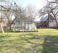 Zahrada rodinného domu v Turanech s houpačkou a skleníkem, obklopená stromy.
