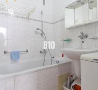 Koupelna ve 3-pokojovém bytě s vanou, umyvadlem, zrcadlem a pračkou.