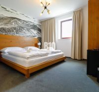 Ložnice v rekreačním apartmánu s dřevěnou postelí a velkoformátovou fotografií krajiny.