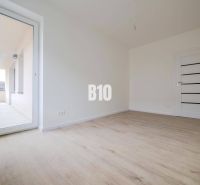 Pokoj s podlahou s dřevěným dekorem a velkými dveřmi na balkon v 3pokojovém bytě.