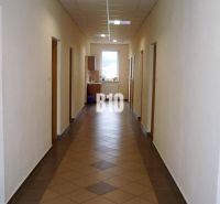 Chodba v kanceláři s dlaždicemi, dveřmi a oknem, interiér osvětlený umělým světlem.
