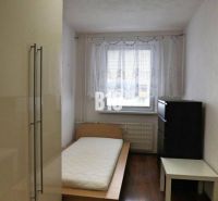 Jednoduše zařízený pokoj s jedním lůžkem a podlahou s dřevěným dekorem ve 4pokojovém bytě.