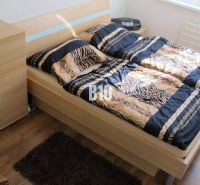 Ložnice se vzorovaným ložním prádlem, komodou a podlahou s dřevěným dekorem ve čtyřpokojovém bytě.