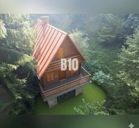 Dřevěná chata v Kuneradě uprostřed lesů s červenou střechou a balkonem.
