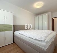 Světlý pokoj v rekreačním apartmánu s postelí, šatníkovými skříněmi a podlahou s dřevěným dekorem.