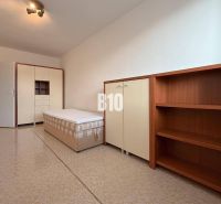 Světlá místnost v Rekreačním apartmánu s postelí, skříní a policovou sestavou.