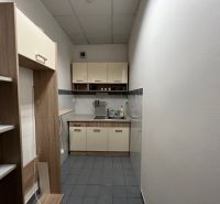 Úzká kuchyňka v kancelářích s jídelním koutkem a regály na skladování.