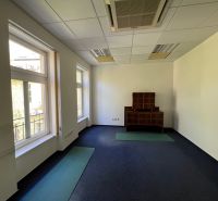 Kanceláře s okny a kobercovou podlahou, s dřevěným nábytkem.