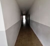 Dlouhá chodba s bílými stěnami a dlaždicovou podlahou v 1-pokojovém bytě.