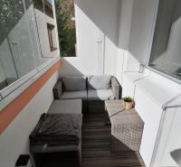 Prosklený balkon s ratanovým nábytkem a podlahou s dřevěným dekorem v 1-pokojovém bytě.