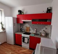 Kuchyně s červenými skříňkami a podlahou s dřevěným dekorem v 1-pokojovém bytě.