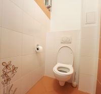 Toaleta s bílými obkladačkami a oranžovou dlažbou v 3-pokojovém bytě.
