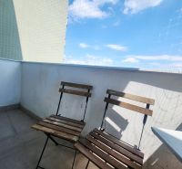 Balkon 3pokojového bytu se dvěma dřevěnými židlemi, modrou oblohou a ochrannou sítí.