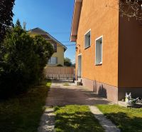 Rodinný dům v Čalovci s oranžovou fasádou, trávníkem a zpevněnou příjezdovou cestou.