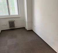 Kancelář s kobercem, radiátorem a oknem se žaluziemi.