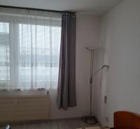Pokoj s postelí, okny a podlahou s dřevěným dekorem ve 2pokojovém bytě.