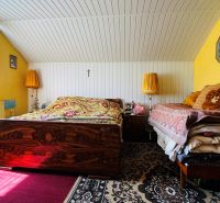 Ložnice v rodinném domě s dřevěným stropem a kobercem, doplněná stolními lampami.