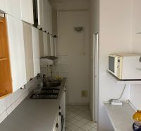 Úzká kuchyně ve 2-pokojovém bytě s bílým nábytkem a dlaždicemi.