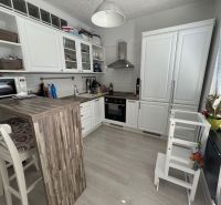 Kuchyně v 2-pokojovém bytě s bílým nábytkem, barovým pultem a podlahou s dřevěným dekorem.