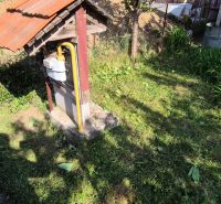 Zahrada rodinného domu v Dedince s trávníkem, plynoměrem a hromádkou země v pozadí.