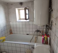 Koupelna v rodinném domě s obklady, vanou a bojlerem.