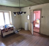 Pokoj v rodinném domě s podlahou s dřevěným dekorem, starší nábytek a okno.