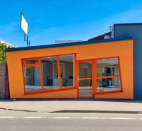 Oranžová fasáda obchodních prostor na Zlatovské ulici v Trenčíně s velkými skleněnými okny.