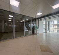 Prosklené obchodní prostory s dlažbou a bankomatem, interiér s velkými okny.