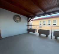 Krytá terasa s hodinami a květináči ve výrobních prostorách.