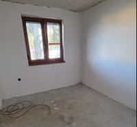 Nedokončený pokoj s oknem v 3-pokojovém bytě, světlá stěna a betonová podlaha.