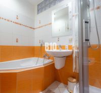 Koupelna v 2-pokojovém bytě s dominantními oranžovými obklady a vanou.