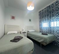 Rekreační apartmán s dvěma jednolůžkovými postelemi, vzorovanými závěsy a stolkem s lampou.