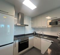 Kuchyně v rekreačním apartmánu s bílými skříňkami, spotřebiči a černou pracovní deskou.